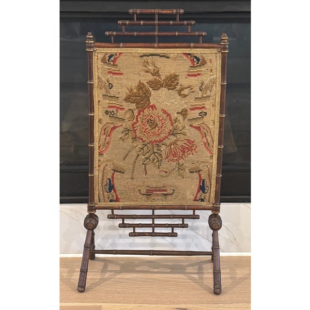 Antique fireplace screen featuring turned faux bamboo wooden frame with warm, aged gilt accents and an inset floral...