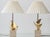 A kindred pair of French sculptural table lamps by Philippe Jean — polished brass bird forms on square travertine bases,...