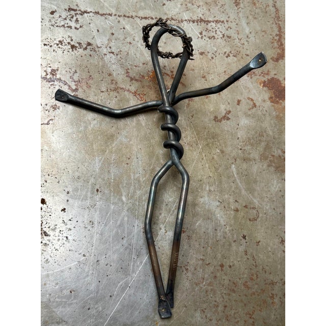 This hand-forged folk art crucifix depicts a stylized Jesus figure formed from solid steel rod, bent and twisted into an...