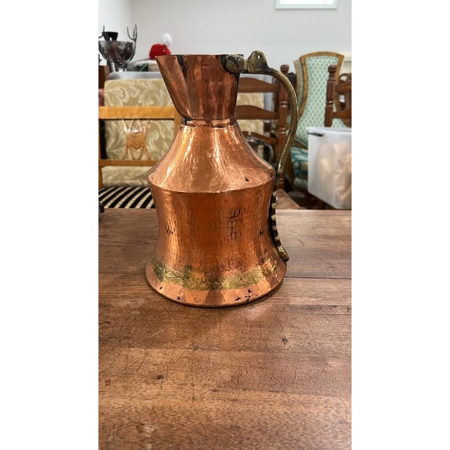 An impressive antique handcrafted pitcher featuring a hand-hammered copper body with rich rustic patina, a flared base,...