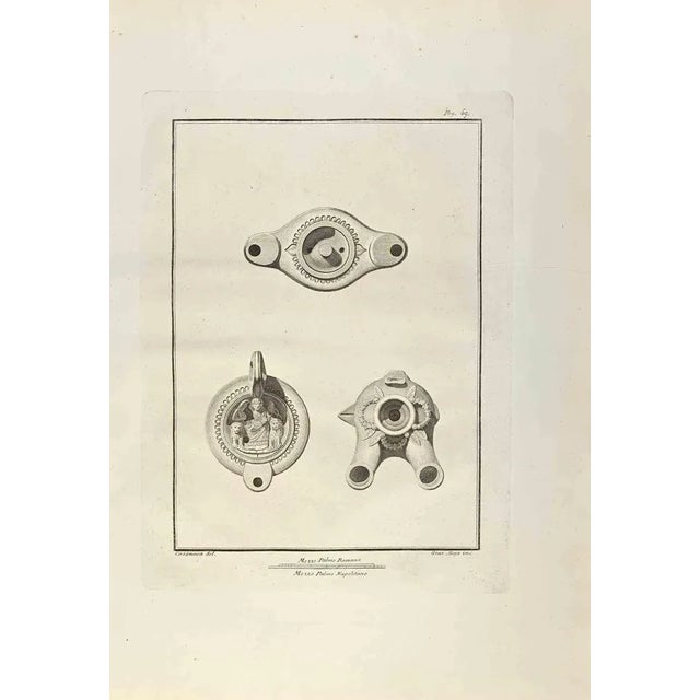 Oil Lamp from "Antiquities of Herculaneum" is an etching on paper realized by Giuseppe Aloja in the 18th Century. Signed...