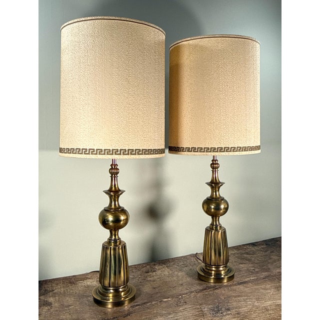 This pair of Hollywood Regency style table lamps features brass bases with tiered baluster form stems including fluted...