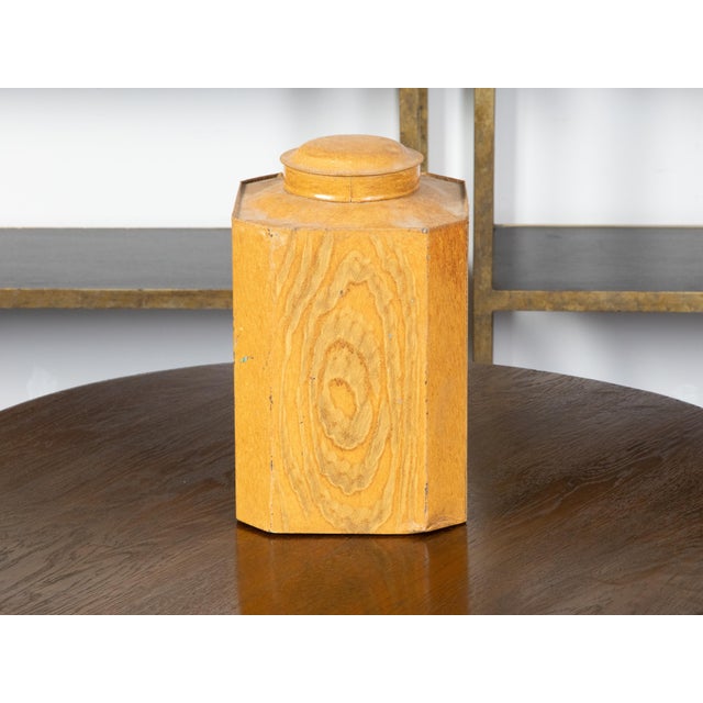 A tin canister from the 19th century, with faux bois finish and canted corners. Created during the 19th century, this...