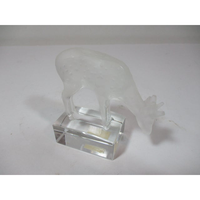 A Lalique crystal sculpted figurine, hand crafted with a frosted crystal deer, grazing on a clear crystal base. It is...