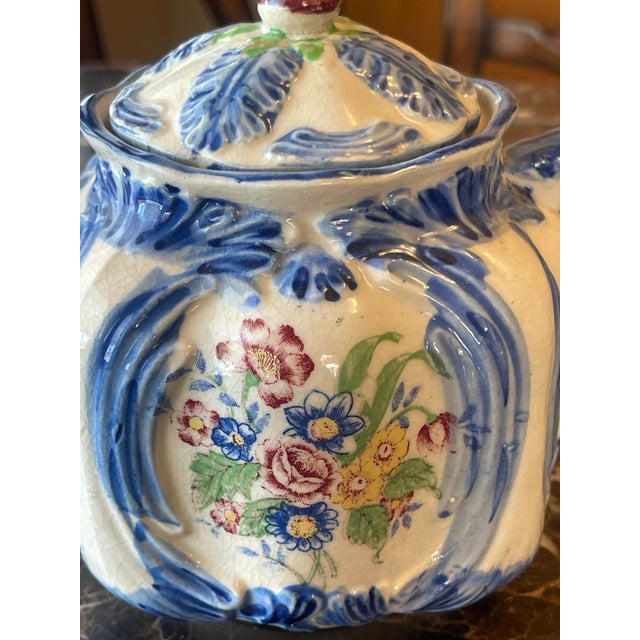 Glazed ceramic floral teapot with decorative lid and blue accents.