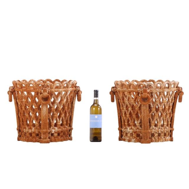A decorative pair of Regency-style cast iron planters featuring pierced latticework bodies, scalloped rims, and...