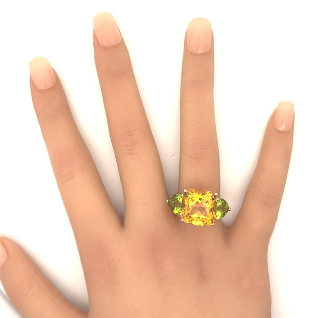 A striking three-stone ring featuring a cushion-cut citrine with a vibrant orange hue. Flanking the citrine are two heart-...