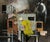 Flood Waters presents a somber narrative through its depiction of a solitary figure in a bright yellow hood, set against a...