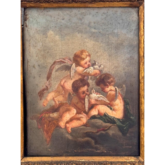 A pair of small framed paintings depicting cherubic figures, each set within an ornate gilt frame in a period style, with...