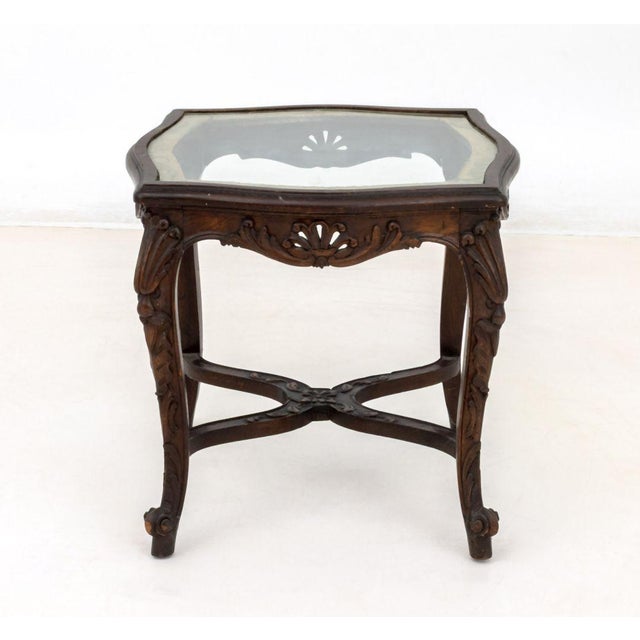 Louis XV Style Glass Top Carved Wood Side Table, circa 1900, with four ornately carved cabriole legs conjoined by an...