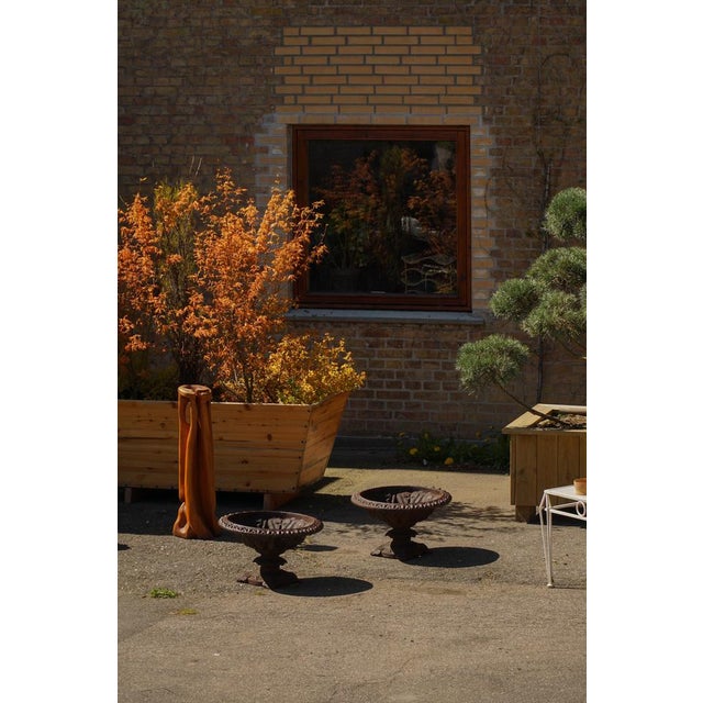 A charming pair of antique garden urns in cast iron, each featuring a richly ornamented rim and a fluted bowl resting on a...