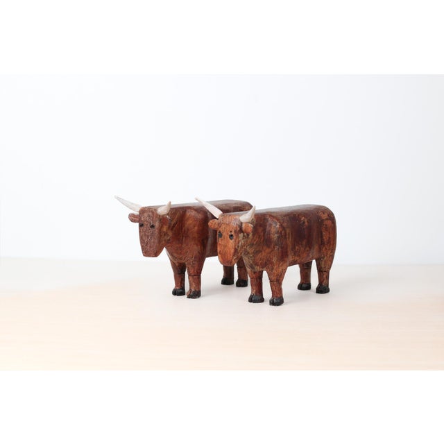 A striking pair of hand-carved wooden bulls, sculpted with bold, minimal forms. Carved from solid wood and finished with...
