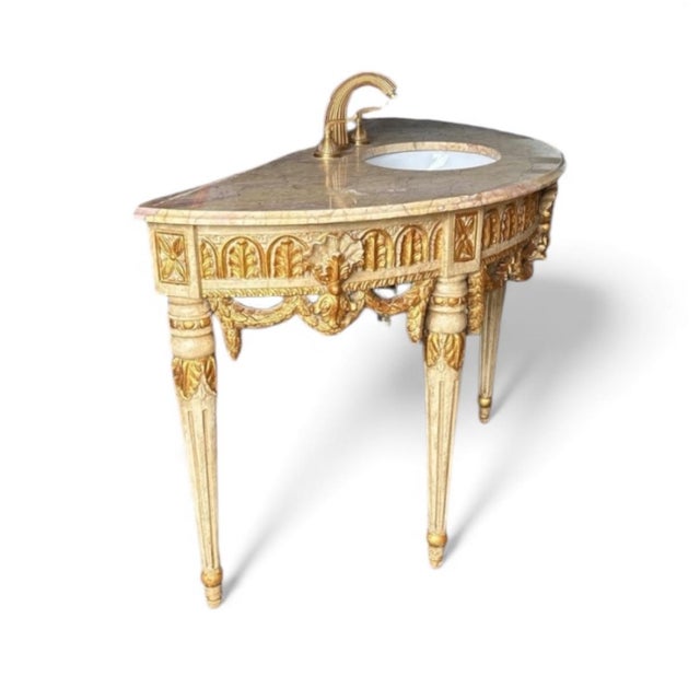 An exquisite Louis XVI–style carved vanity finished in pale cream with gilded accents and topped with a breathtaking...