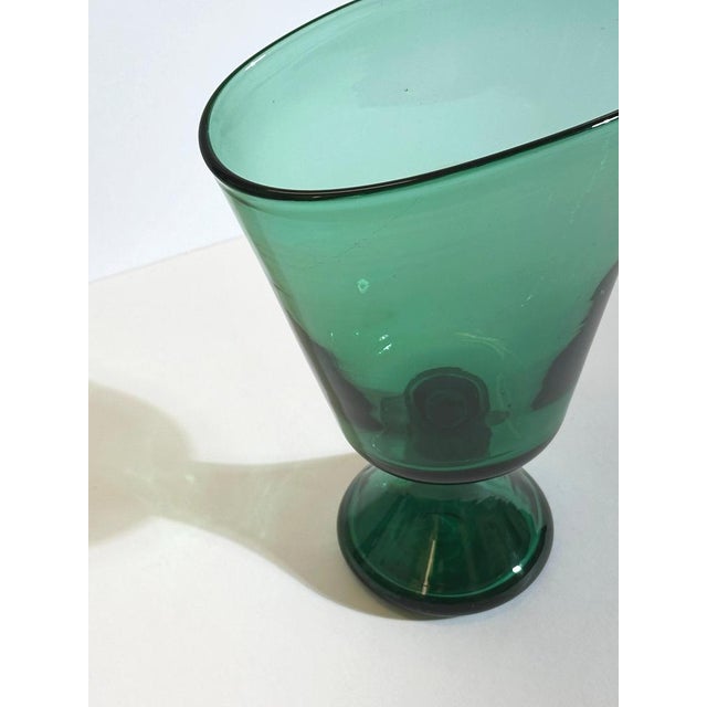 This green blown glass pedestal vase by Vetro Verde di Empoli, produced in Italy circa the 1950s, demonstrates a fluid...