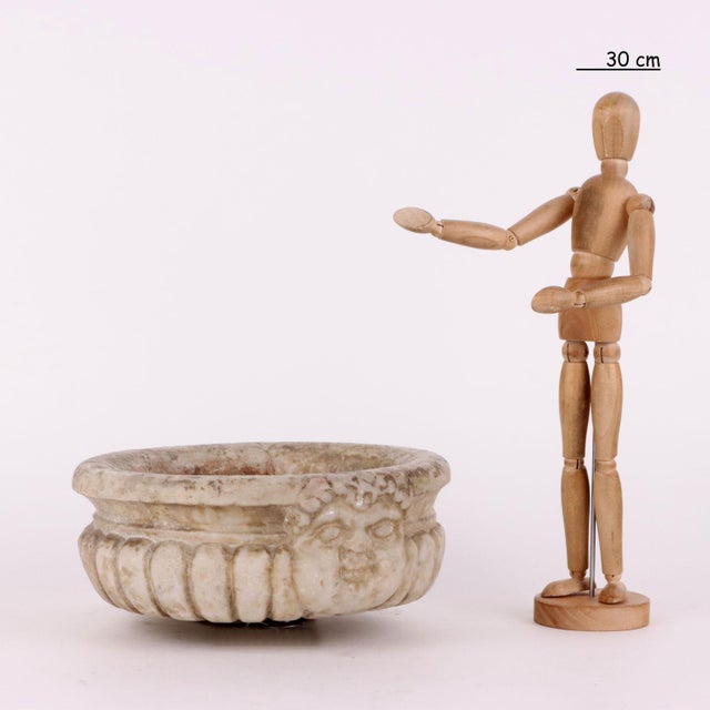 Circular marble bowl shaped like a pod. On the front, a finely sculpted face. This piece is attributed to the mentioned...
