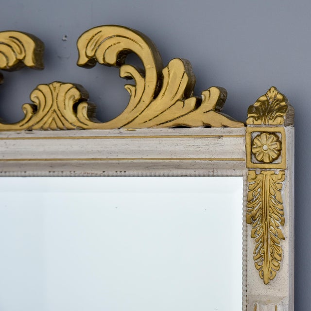 An elegant mid-century wall mirror in the French Neoclassical taste, featuring a cream-painted carved wood frame with gilt...