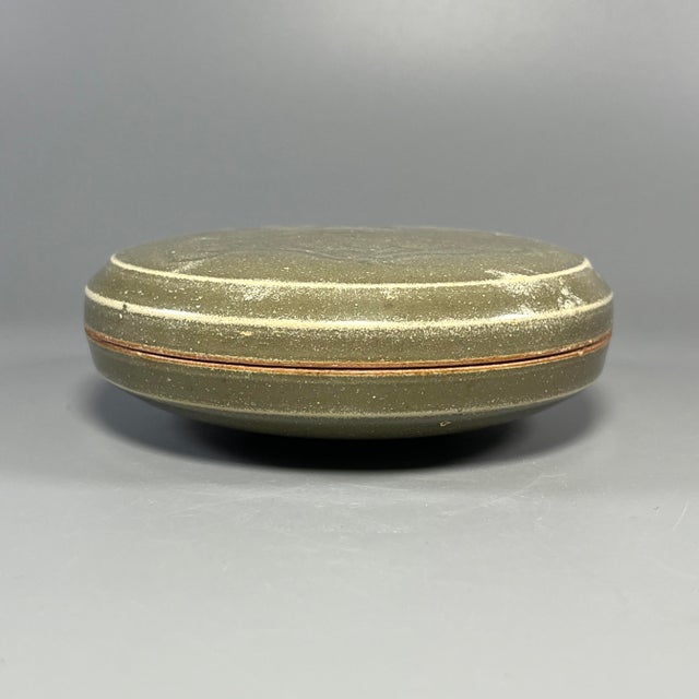 A vintage‑style Chinese Longquan celadon circular lidded box, beautifully carved with floral motifs on the top surface. It...