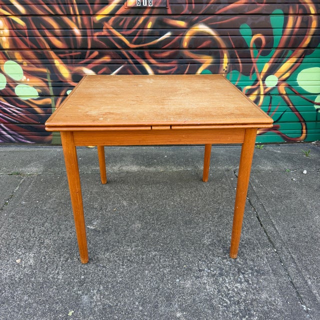 A classic Danish Modern teak dining table featuring a square top with two convenient pull-out leaves that extend from...