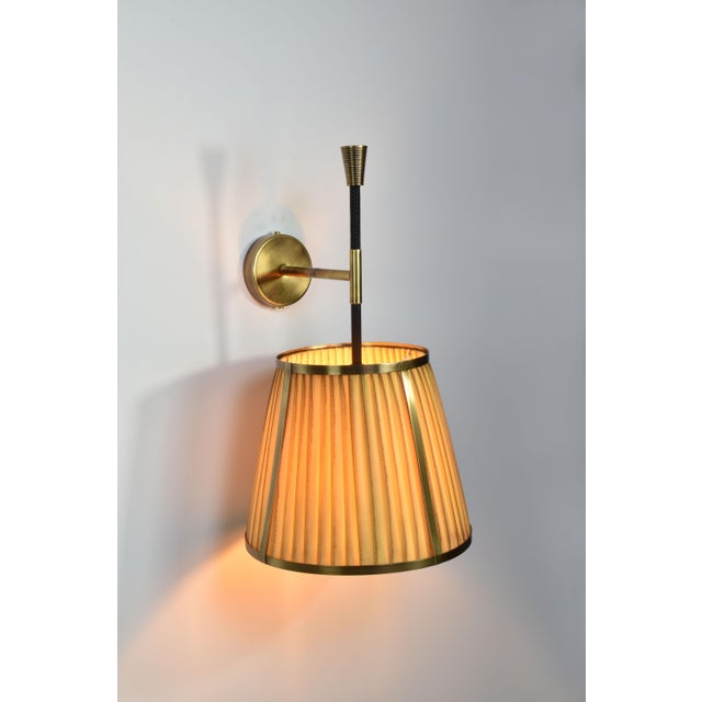 The handcrafted Caeli-w4 wall light, combines a modern brass structure with a unique, hand-dyed pleated fabric shade. The...