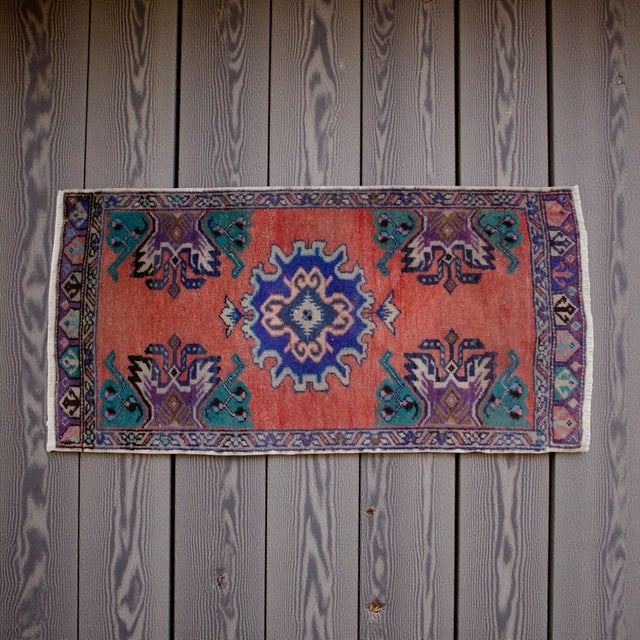 This charming vintage Oushak mat features a vibrant terracotta field contrasted by deep indigo and teal accents, creating...