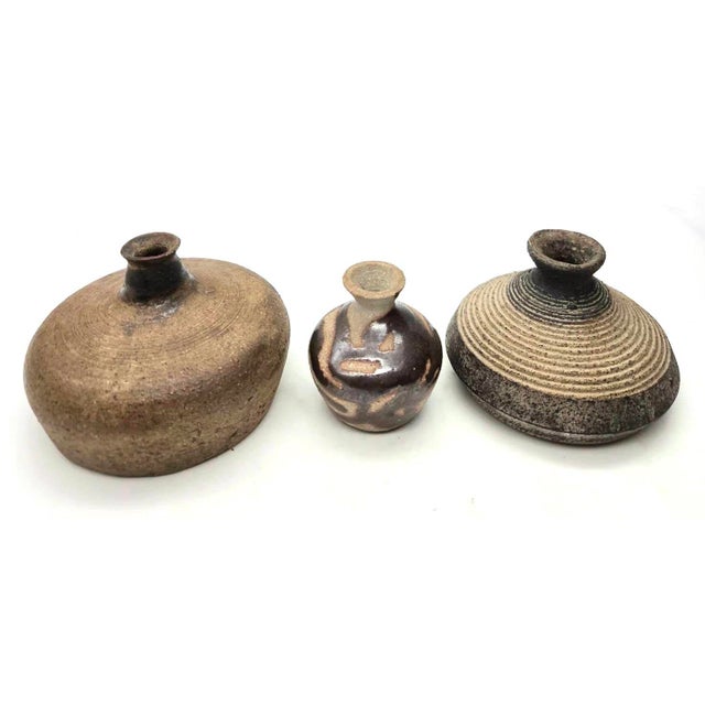 Offered are 3 studio pottery stoneware bud vases crafted from clay with earth-tone glazes such as a dark iron or plum-...