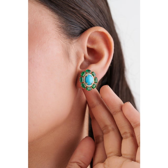 These retro style floral cluster stud earrings feature a vibrant 6.53ct Turquoise & Emerald, set in 14k yellow gold. The...