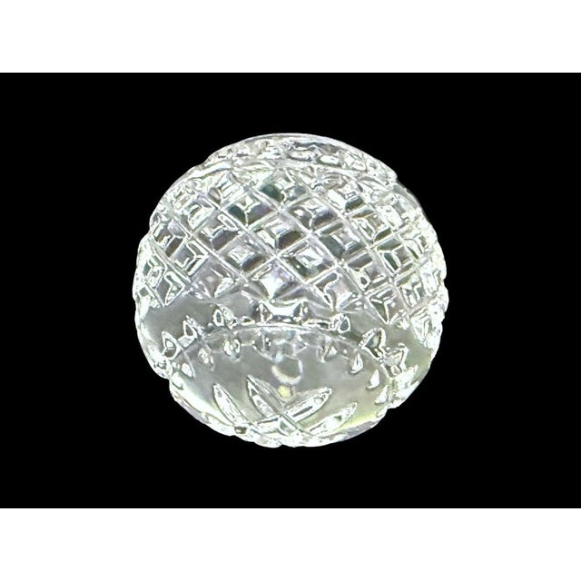 A luminous Waterford crystal paperweight with a rounded, faceted profile, cross-cut diamond detailing, and a starburst-cut...