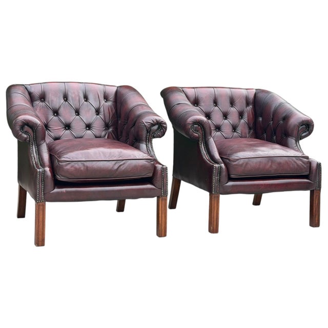 A classic pair of vintage Chesterfield club chairs upholstered in rich oxblood leather, featuring deep button-tufted...