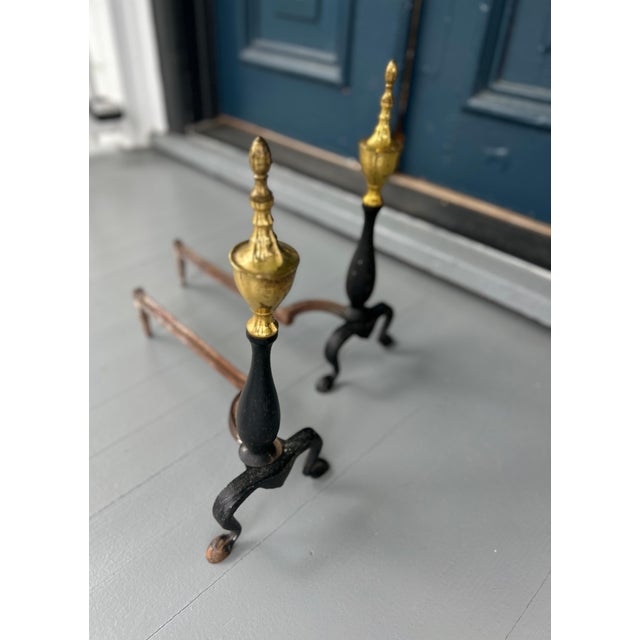Elegant pair of Federal style antique andirons featuring classic brass urn finials atop turned black iron shafts, raised...