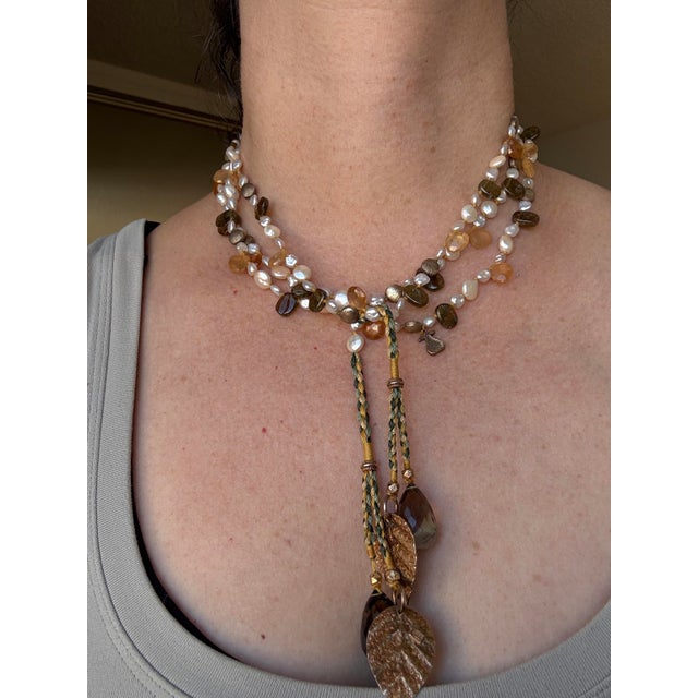 A beautiful handcrafted multi-strand necklace featuring a warm, natural mix of stones and textures. Braided silk gold-tone...