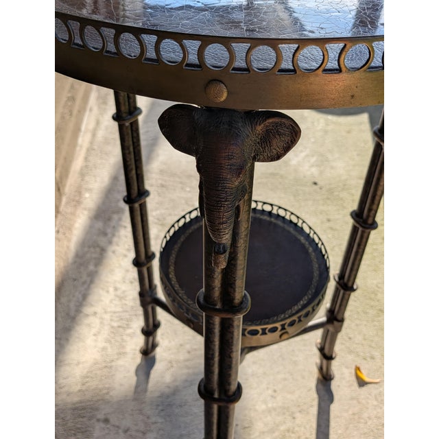 Two tier round accent table with three metal faux bamboo brass legs and elephant heads decor. The table has a leather top.
