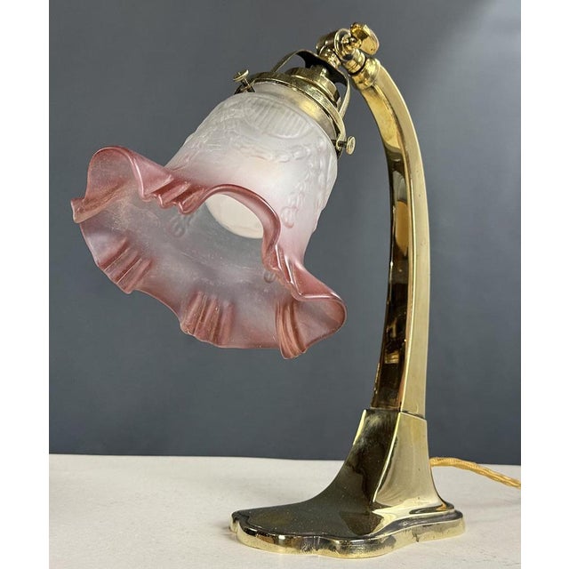 An elegant Art Nouveau table lamp with a polished brass structure. The frosted glass shade features a rich embossed...