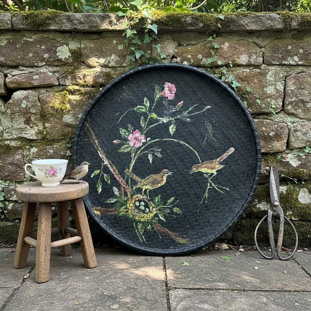 Substantial hand-painted rattan tray featuring a delicate bird and floral design set against a deep black woven ground,...