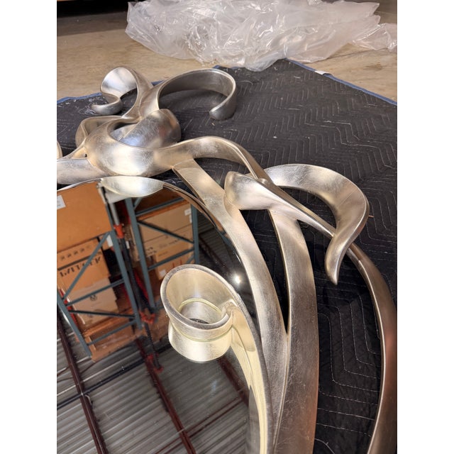 Contemporary sculptural mirror featuring an eye-catching frame of flowing, ribbon-like forms finished in a soft champagne...