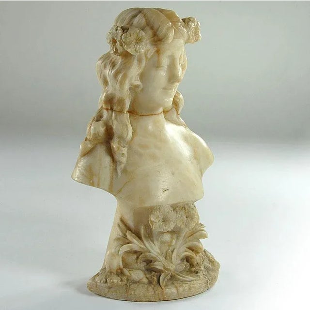 A bust of girls with a delicate beauty handly carved in marble with a warm color. Anatomical details and floral...