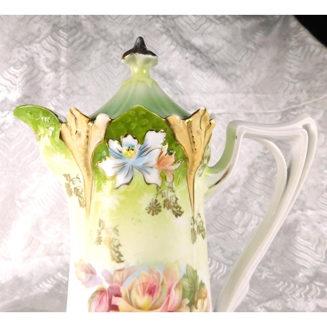 This is an unmarked chocolate pot in white and green with pink and yellow flowers on the front, peach and purple...