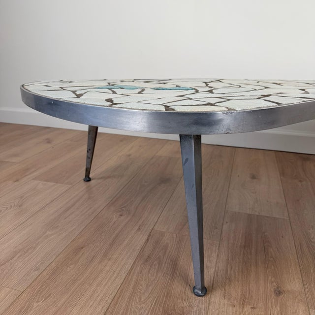 A sculptural mid-century coffee table with a flowing, kidney-shaped silhouette and mosaic glass tile top. The surface...