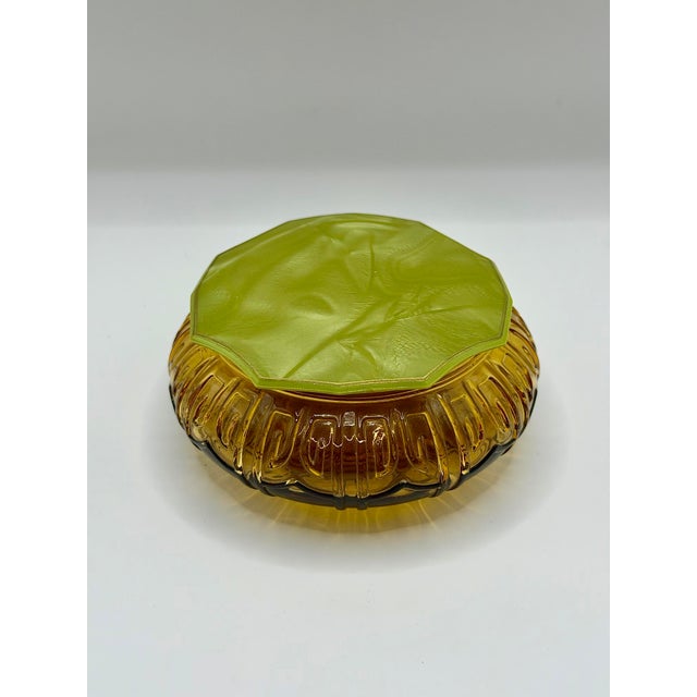 A striking vintage amber glass vanity jar with a chartreuse green molded lid. The base is made from heavy pressed glass...