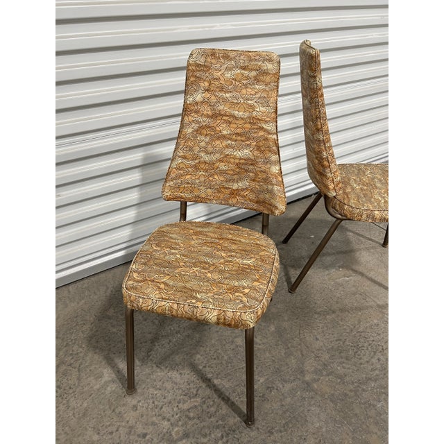 This pair of vintage mid-century modern dining chairs feature original vinyl upholstery and copper coated legs offering a...