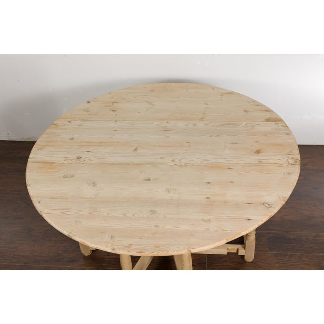 An English rustic pine drop leaf table from the 19th century with oval top, two drop leaves, carved apron, turned legs,...