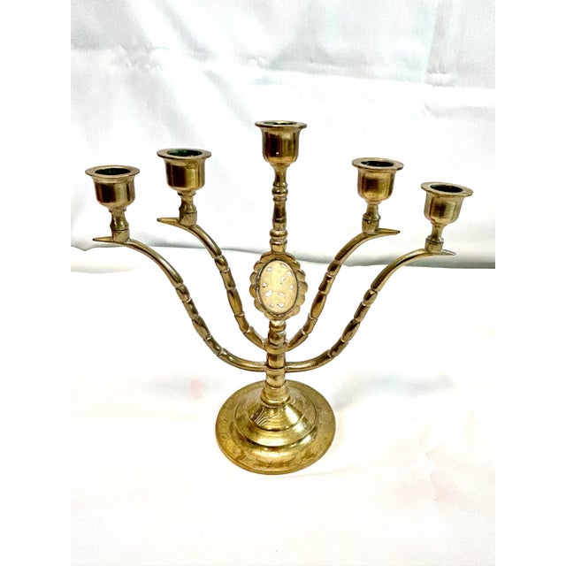 An elegant pair of Hollywood Regency brass candelabras featuring sweeping five-arm silhouettes and carved bone medallion...