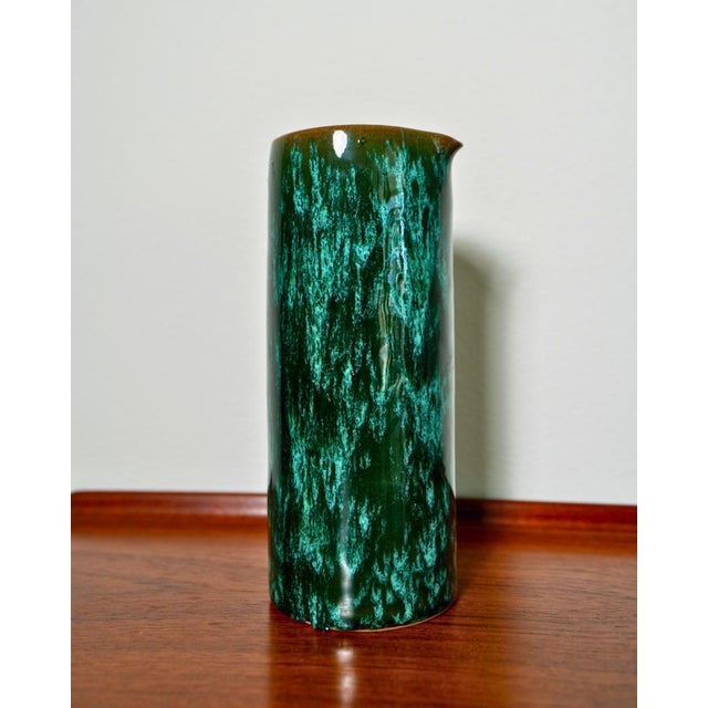 A striking contemporary ceramic pitcher or vase with a deep emerald and black mottled glaze that reads almost like...