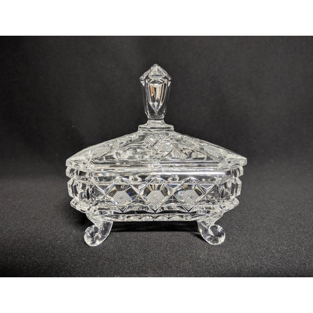 A striking lidded cut crystal candy dish with feet. The rectangular dish features four curved feet, a tall steeple finial,...