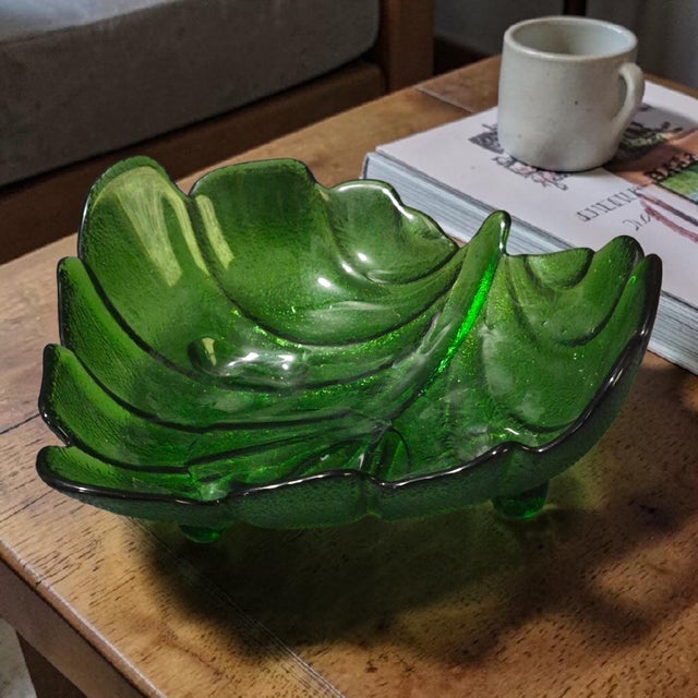 This Vintage Forest Green Glass Leaf Shaped Footed Candy Dish is a charming and unique piece for serving and displaying...