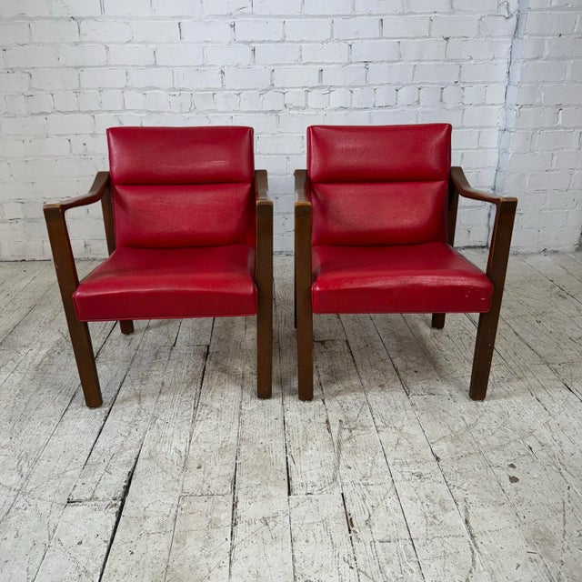Pair of mid century modern arm chairs. This chairs feature a red vinyl seat and back and a walnut wood frame. This set...