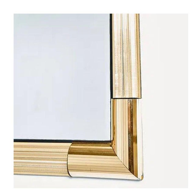 A Mid-Century Modern square wall mirror framed in polished gold tone metal and clear lucite rod accents. The layered,...
