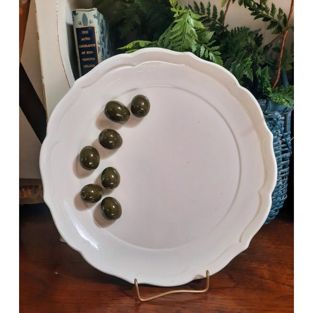 this trompe l’oeil plate is topped with seven sculpted ceramic olives that appear to rest directly on the surface. Rooted...