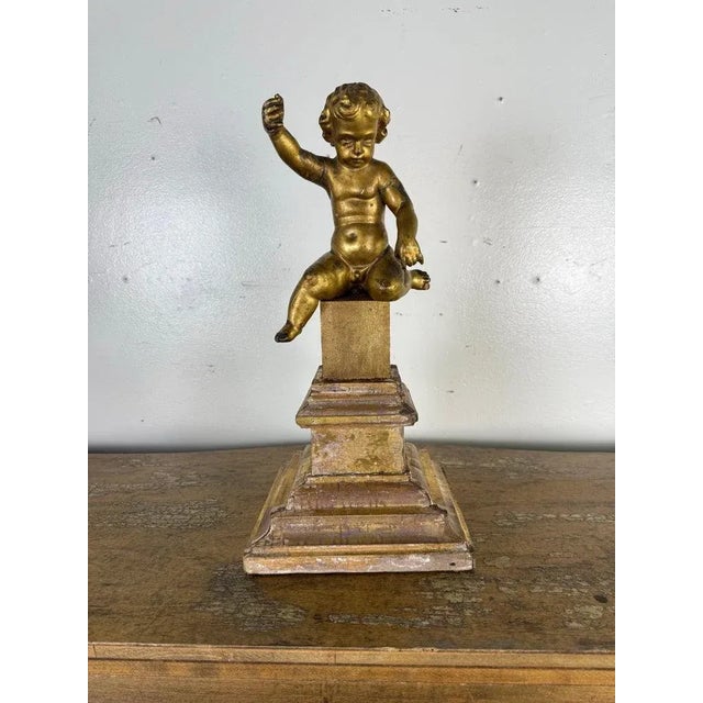 An exquisite 19th-century Italian giltwood cherub figure, beautifully hand-carved and seated atop a stepped architectural...