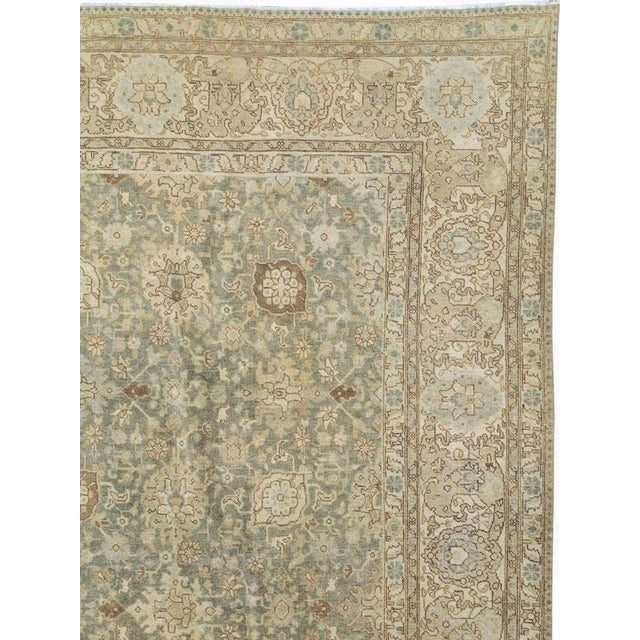 This early 20th-century Persian Tabriz carpet presents a refined allover floral composition across a soft blue-green...