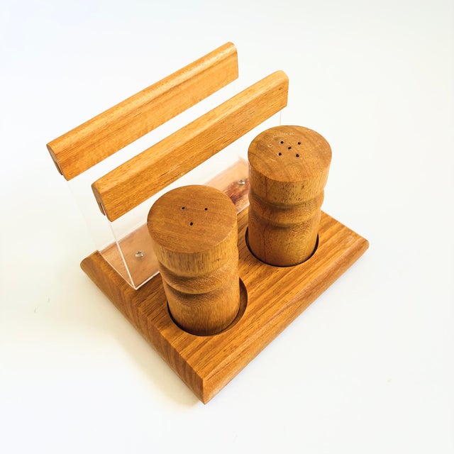 A vintage wood salt and pepper shaker and napkin holder set. 2 wood salt and pepper shakers sit neatly in circular grooves...